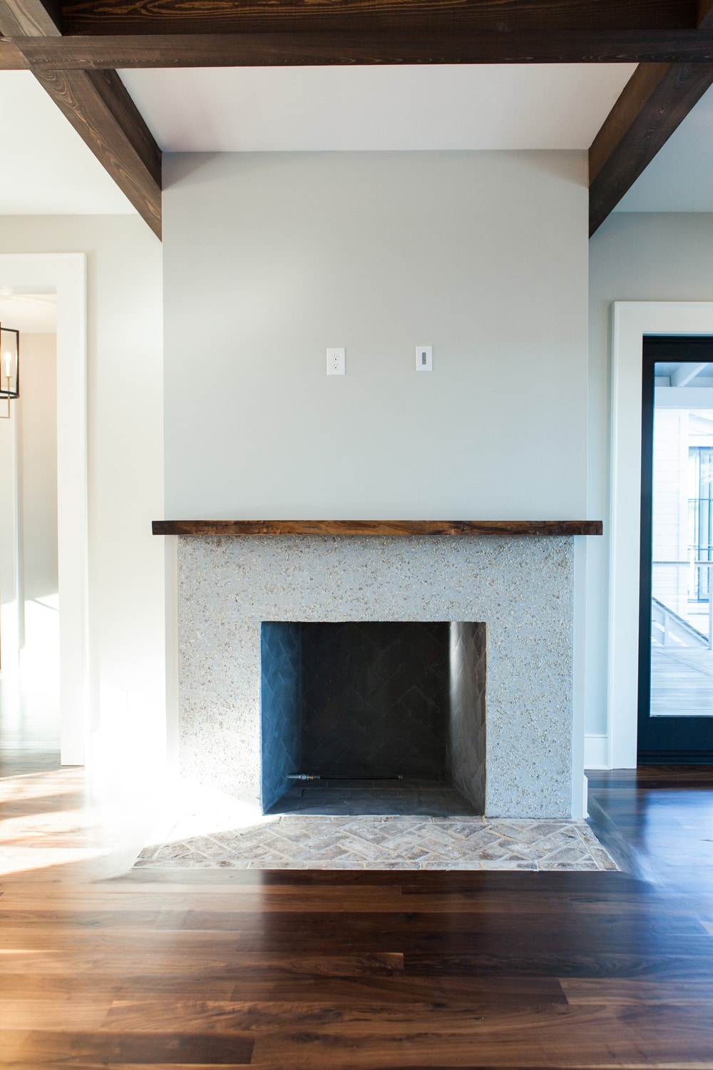 Fireplace wall features tabby stucco surround with brick herringbone hearth and reclaimed walnut mantle inside of Custom Johns Island Home